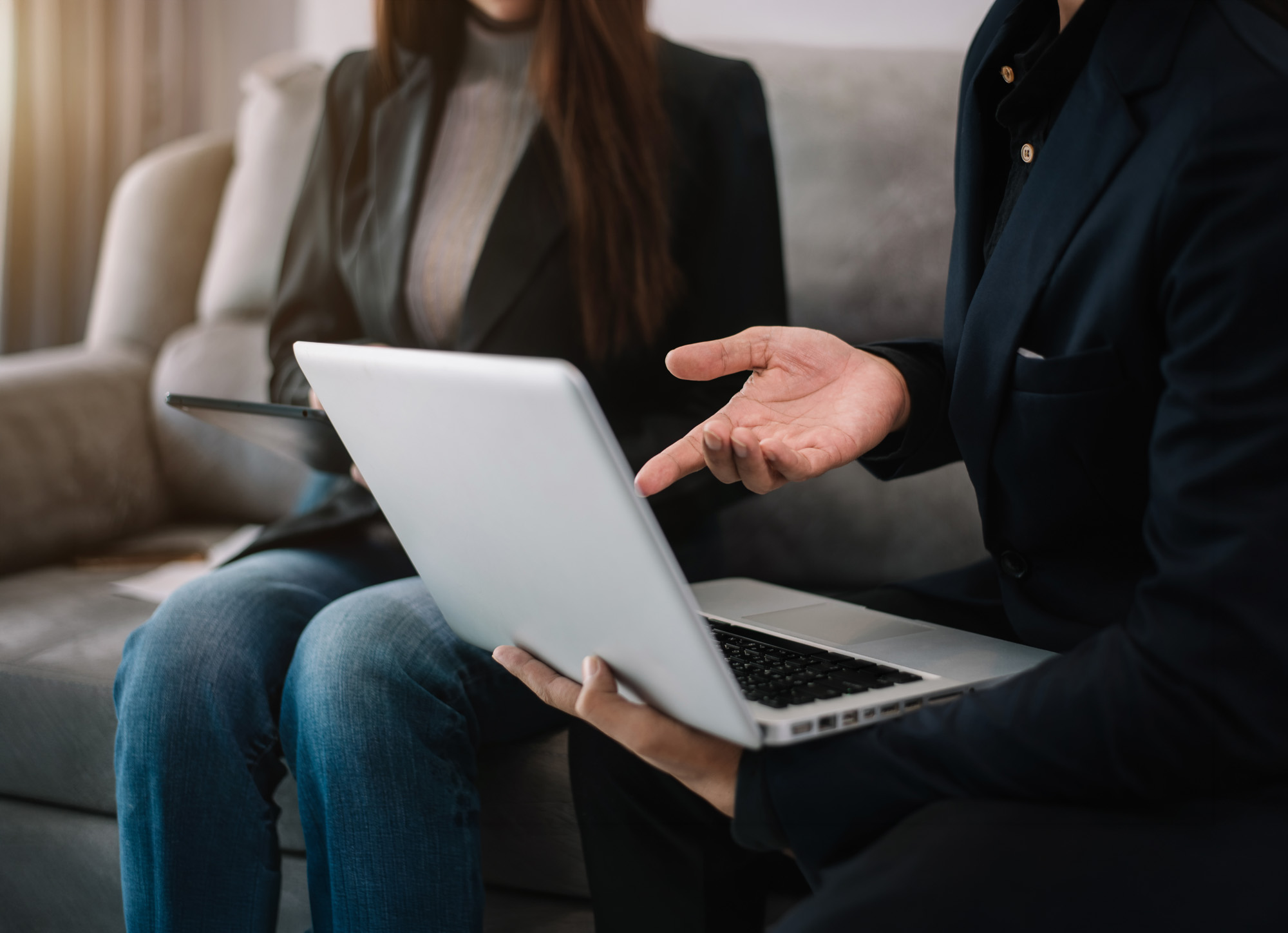Two people sit on a couch discussing something on a laptop screen.