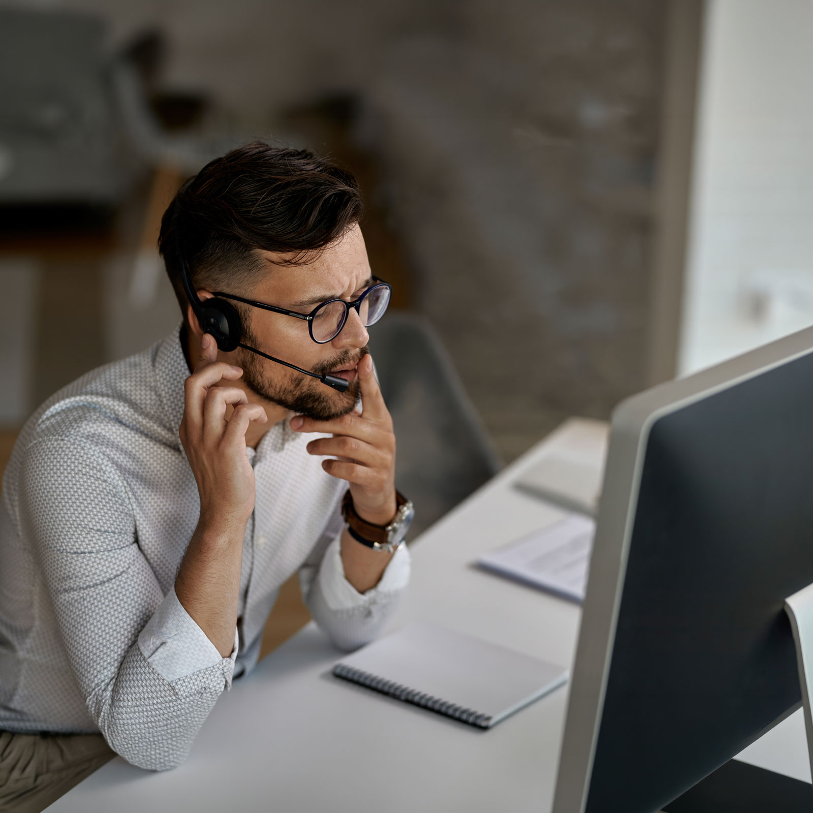 A man wearing a headset is working at a computer, appearing focused and attentive.