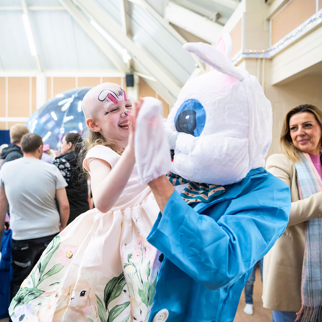 A person in a bunny costume holds up a smiling child with face paint in a crowd.