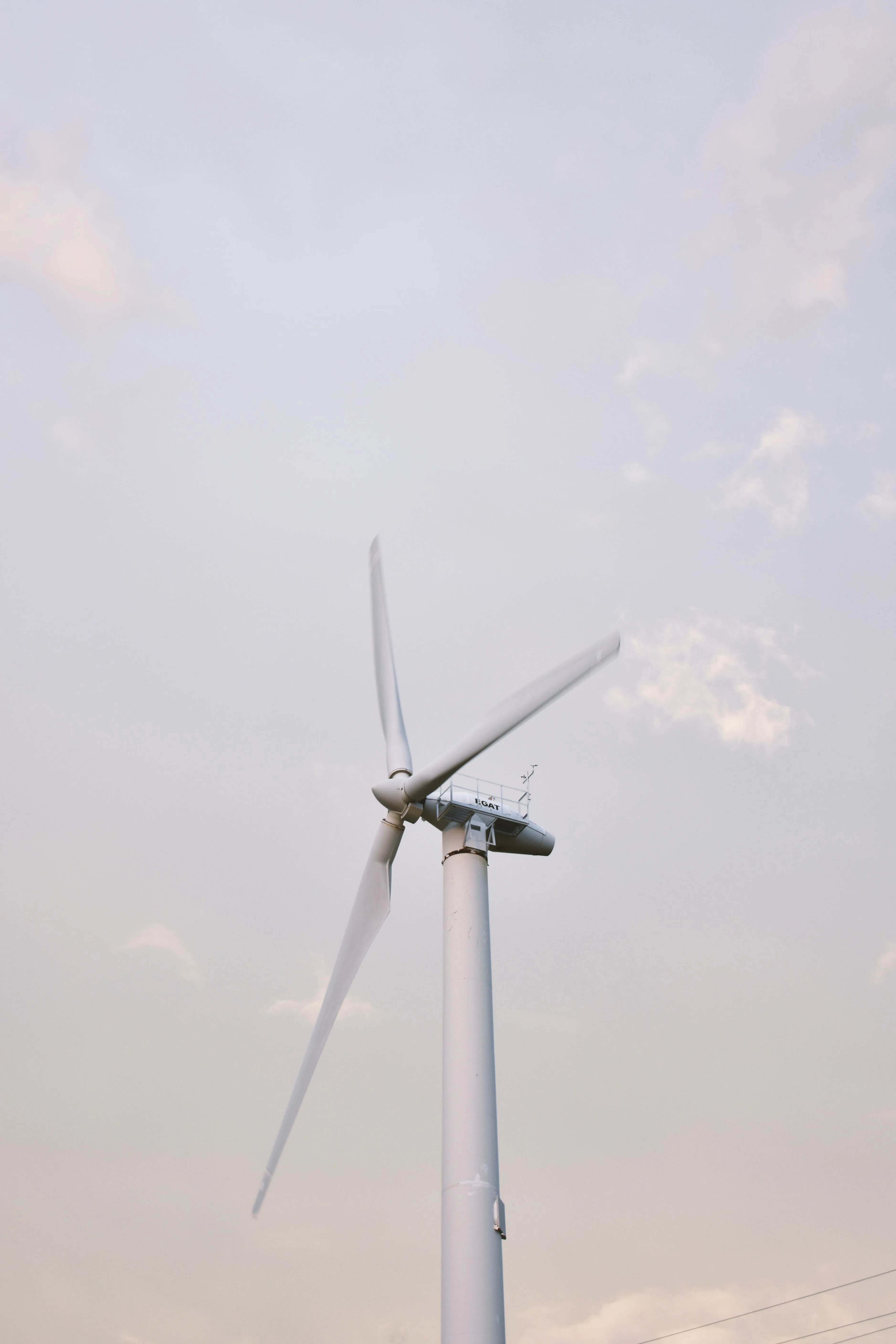 Close-up of a white wind turbine with spinning blades against a cloudy sky.