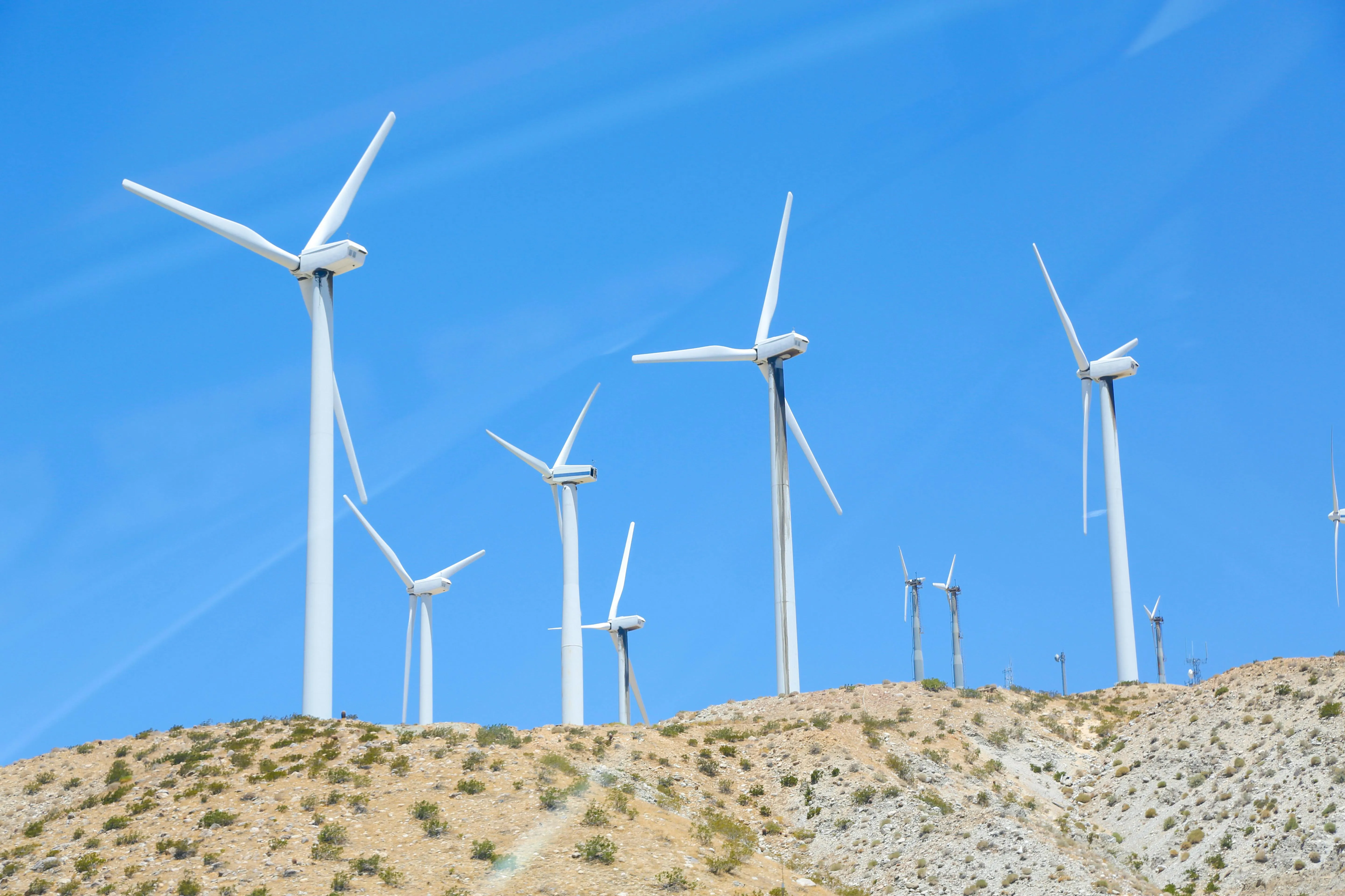 Several white wind turbines on a dry hill under a clear blue sky.