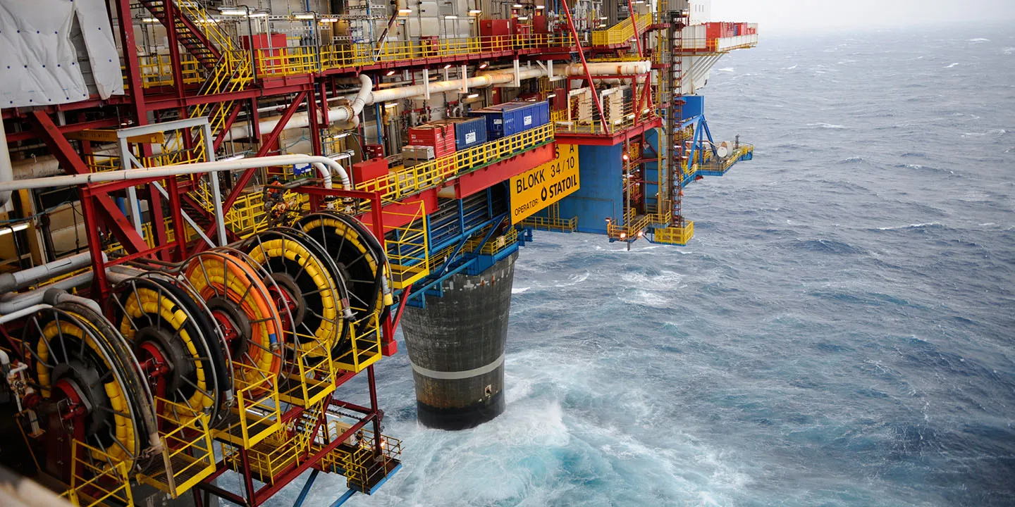 Close-up view of an offshore oil platform structure with large cable reels and the ocean in the background.