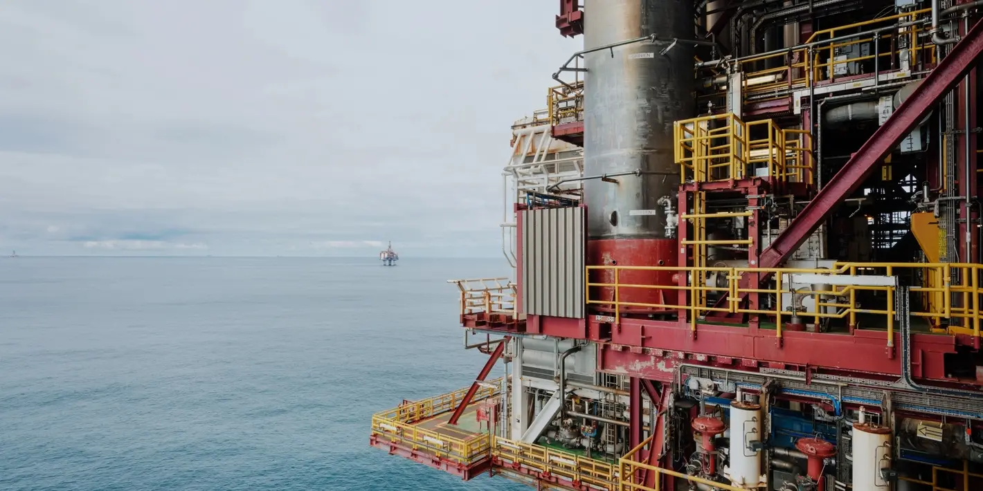 Close-up of an offshore oil platform structure above the ocean with another platform visible in the distant sea.