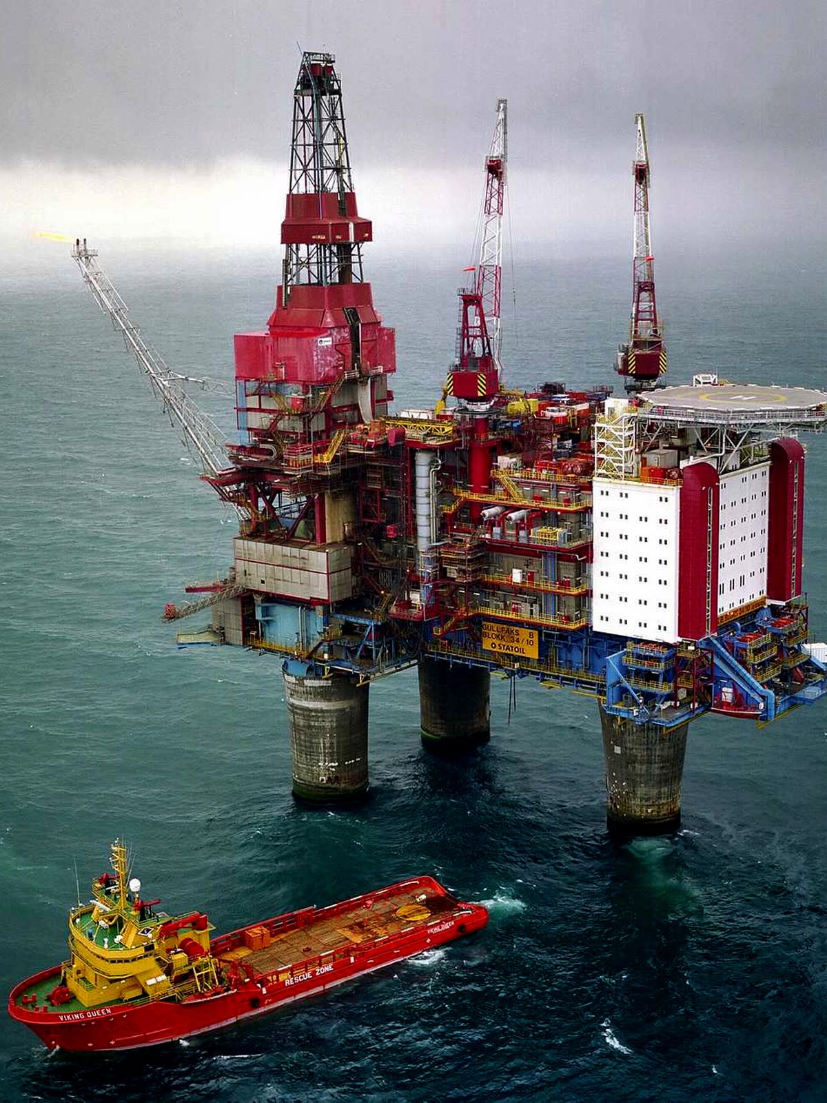 Offshore oil rig in the ocean with an accompanying red and yellow supply vessel named Viking Queen.