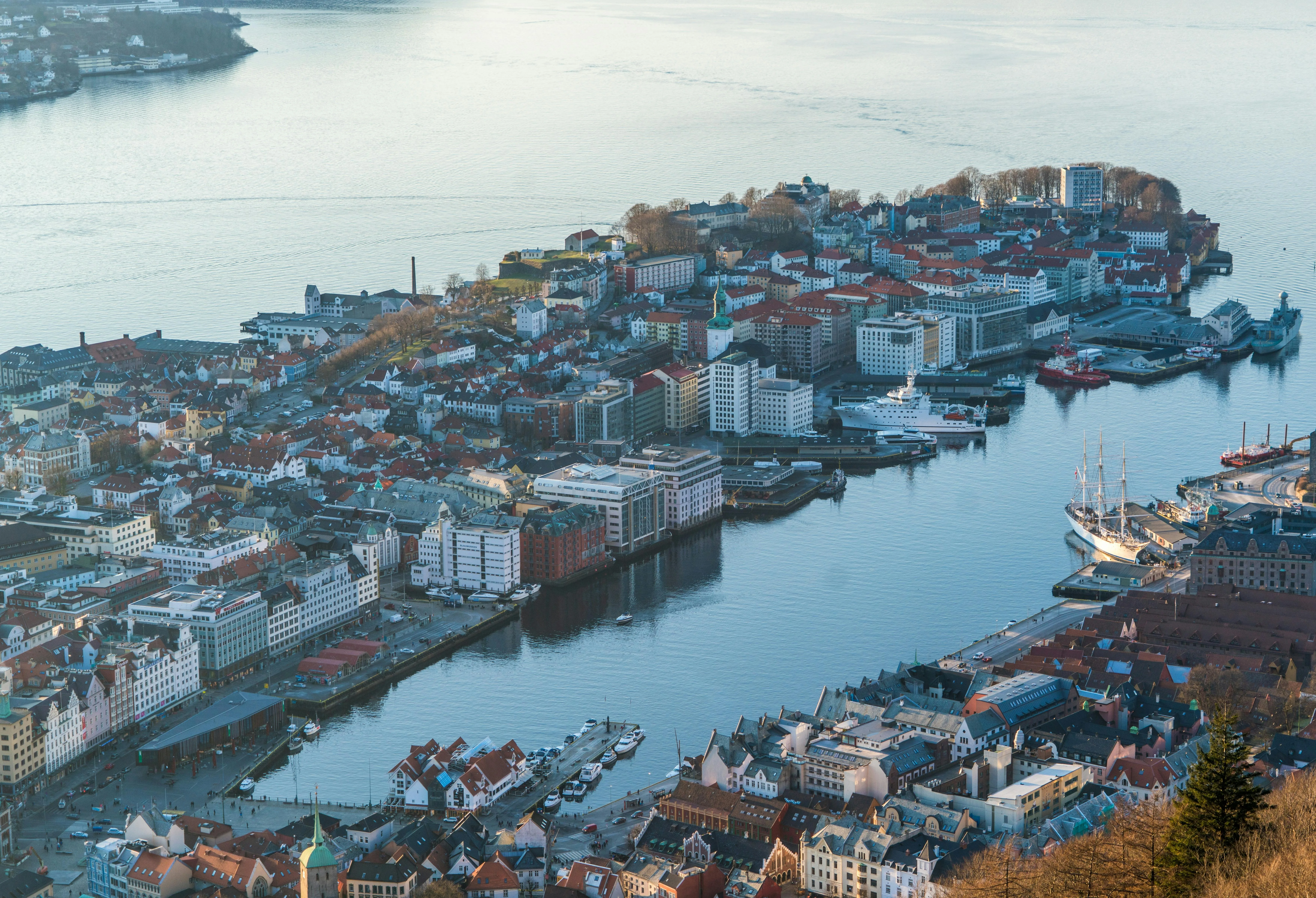 Aerial view of a coastal city with densely packed buildings, a harbor with boats, and calm water.