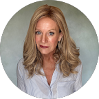 Portrait of a woman with long blonde hair wearing a white shirt and posing against a neutral gray background.