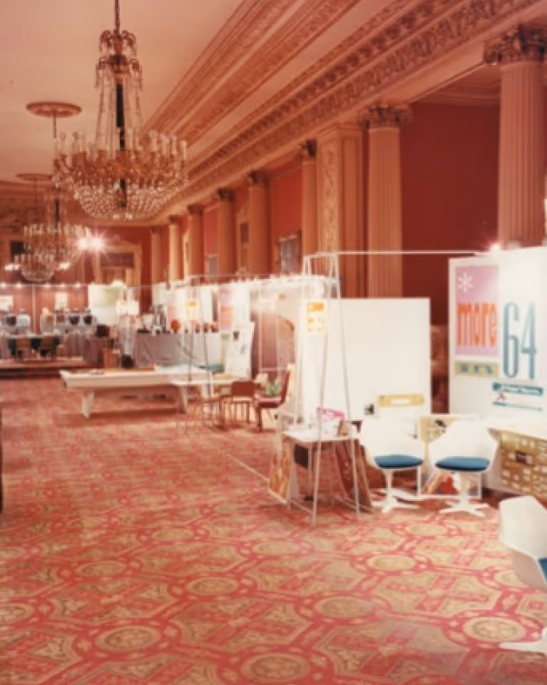 Ornate hall with chandeliers hosting a retro-style exhibition with booths and vintage decor.
