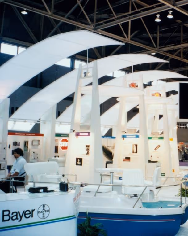 Bayer booth with white structures and seating at an indoor trade show or expo.