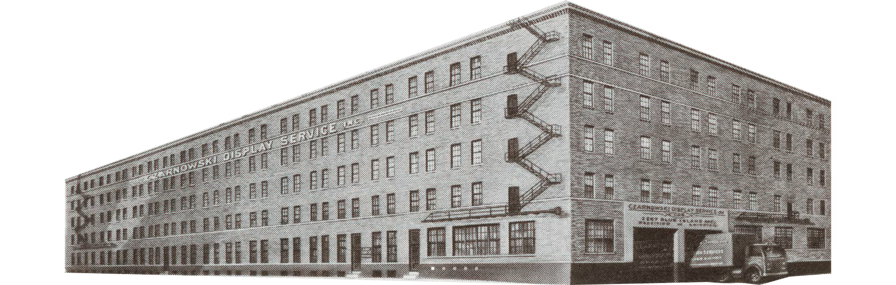 Black-and-white photo of a large multi-story industrial building with windows and fire escapes.