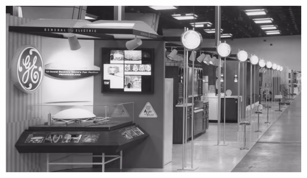 Black and white photo of General Electric World's Fair pavilion with displays and lights in a large exhibition hall.