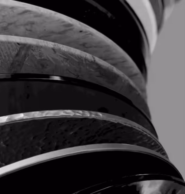 Close-up of curved, polished stone and metal layers stacked vertically with textures and reflections.