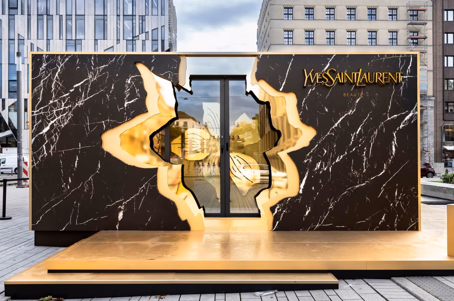 Yves Saint Laurent store entrance with black marble and gold leaf design in urban setting.
