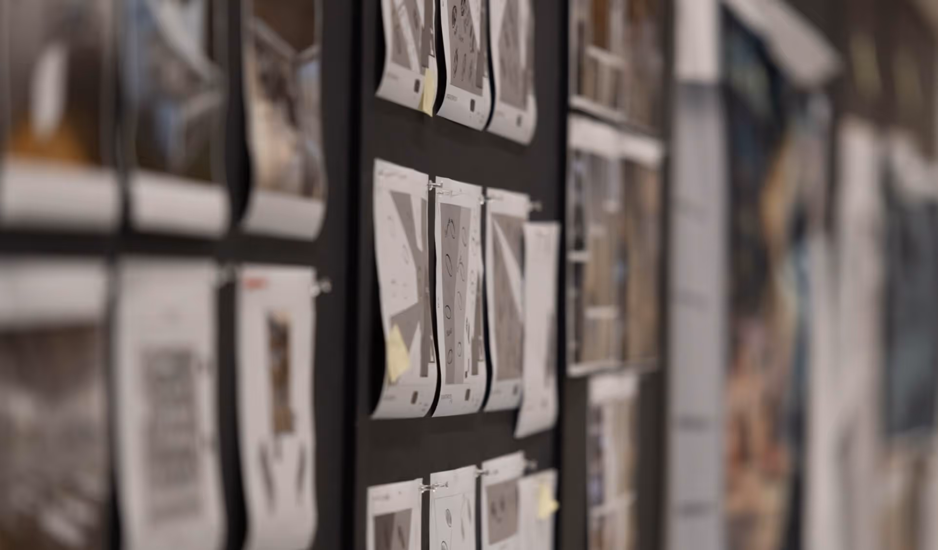 Wall with pinned papers and sketches arranged in rows, slightly curled at the edges.