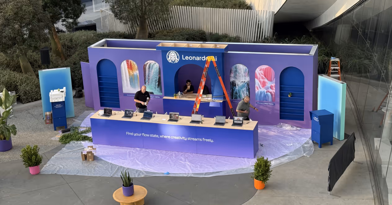 Purple exhibition booth with laptops on front counter, posters of waterfalls, and two men setting up.
