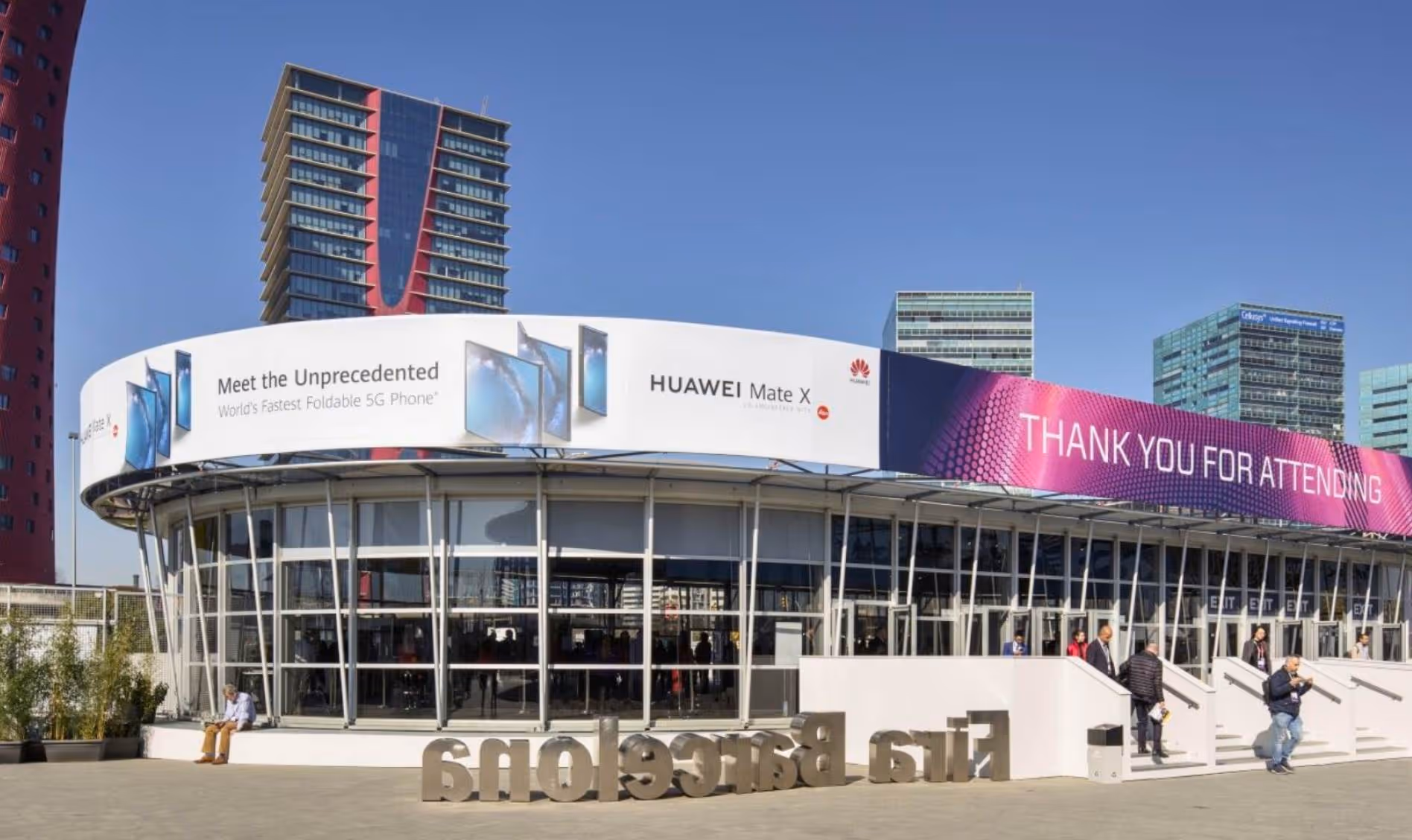 Modern round building with Huawei Mate X 5G phone ads and a 'Thank you for attending' banner in a city plaza.