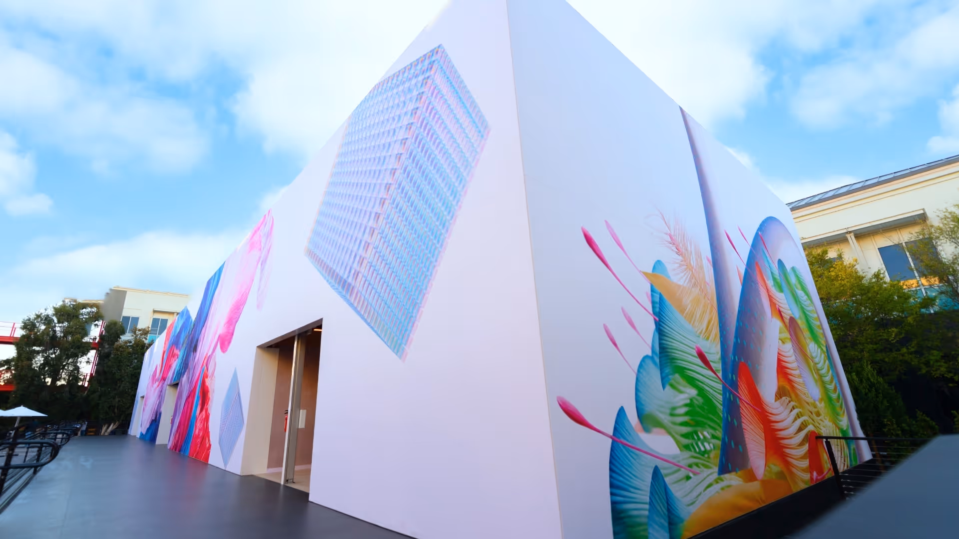 White building corner with colorful abstract murals including geometric shapes and organic forms.