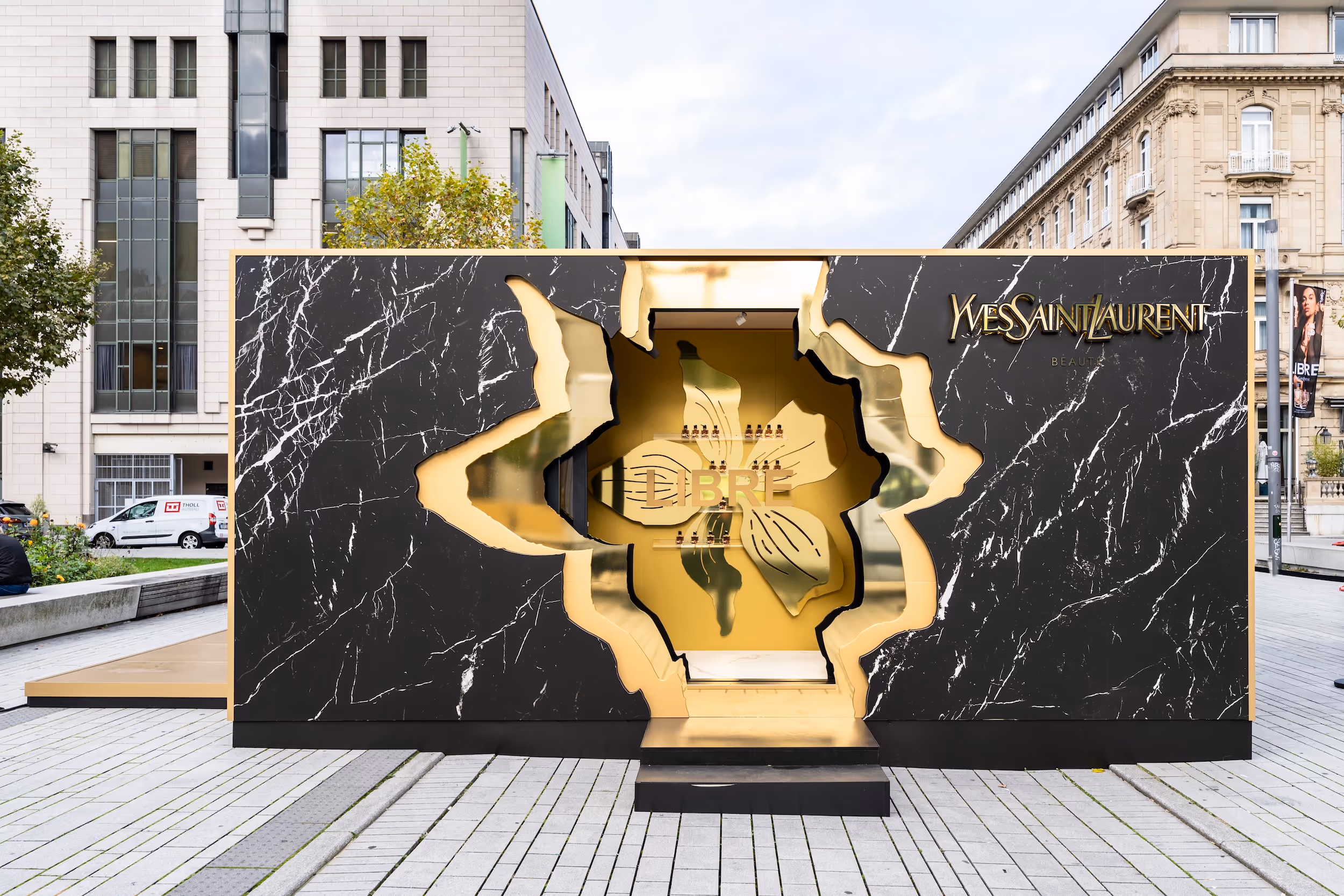 Yves Saint Laurent Beauty display with black marble and gold interior shaped like a flower on city street.