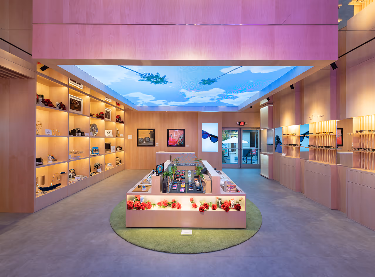 Modern showroom with wood shelves, glasses displays, and a ceiling screen showing sky with palm trees.