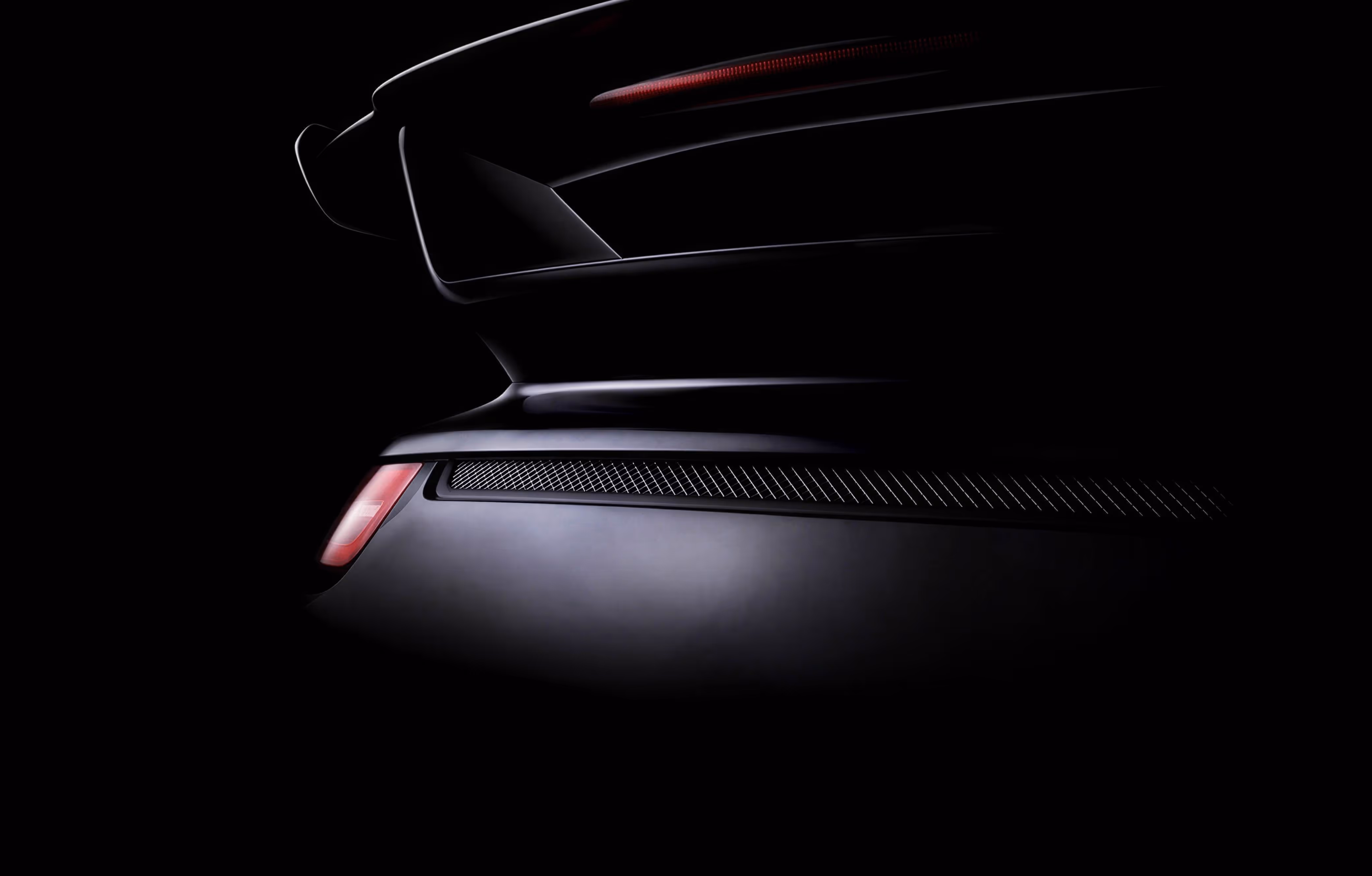 Rear end of a sleek black sports car with illuminated brake light against a dark background.