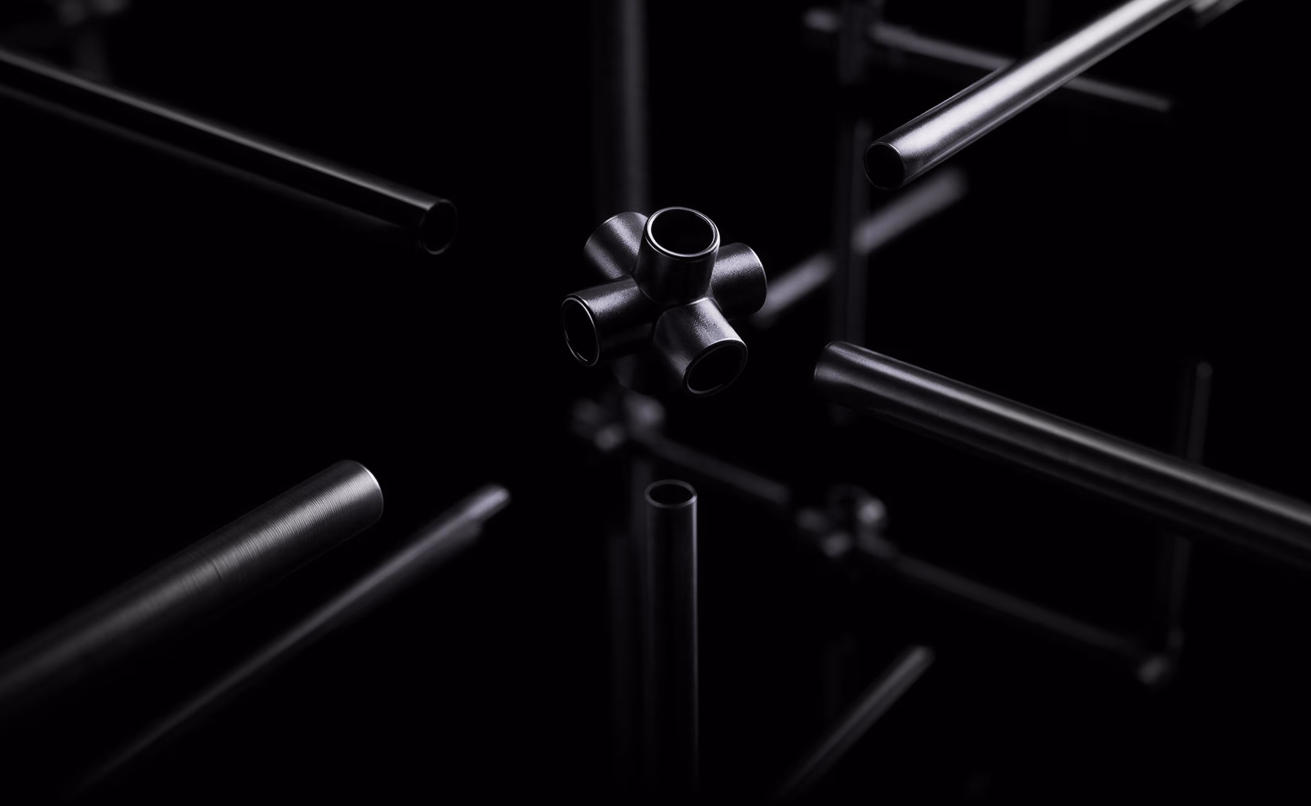 Black metallic pipes and a multi-directional connector against a black background.