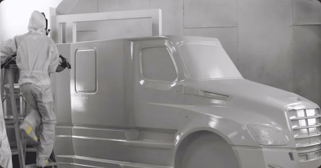 Person in protective gear spray painting a large vehicle model indoors.