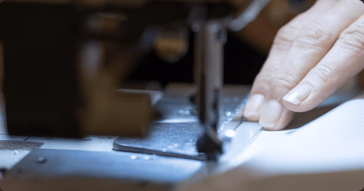 Close-up of a hand guiding white fabric on a sewing machine for stitching.