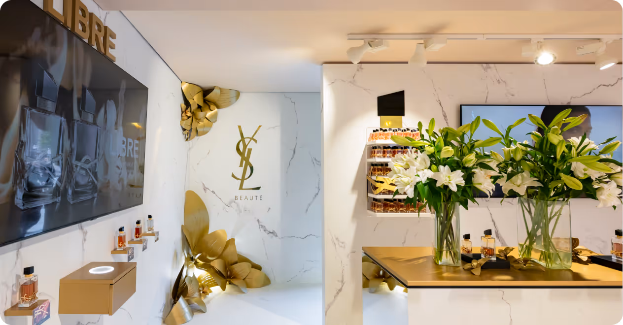 Luxurious YSL Beauté display with white lilies, marble walls, and gold accents in a bright retail space.
