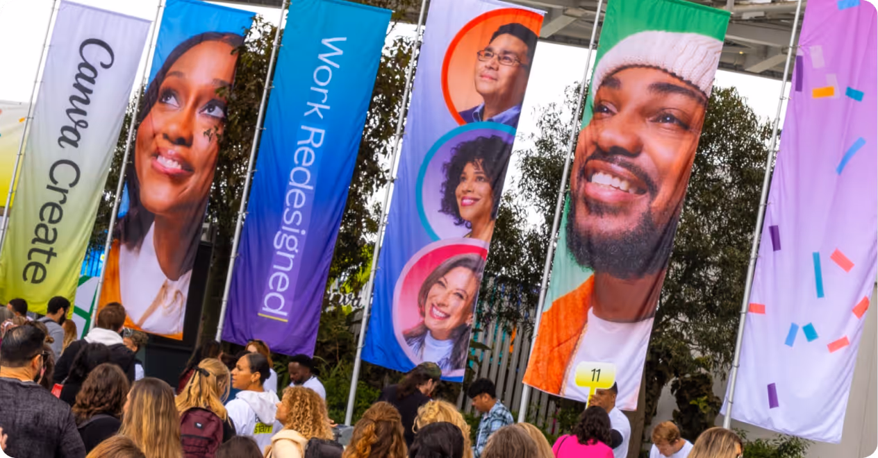 Colorful vertical banners with smiling faces and words like Canva Create and Work Redesigned at an outdoor event.