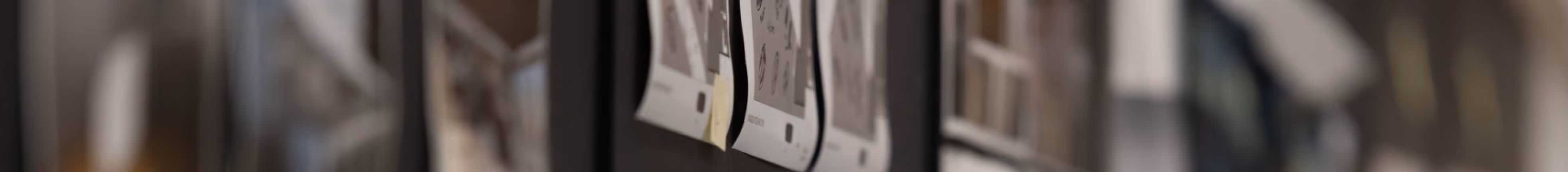 Blurred wall with pinned sketches or printed designs in a creative workspace.