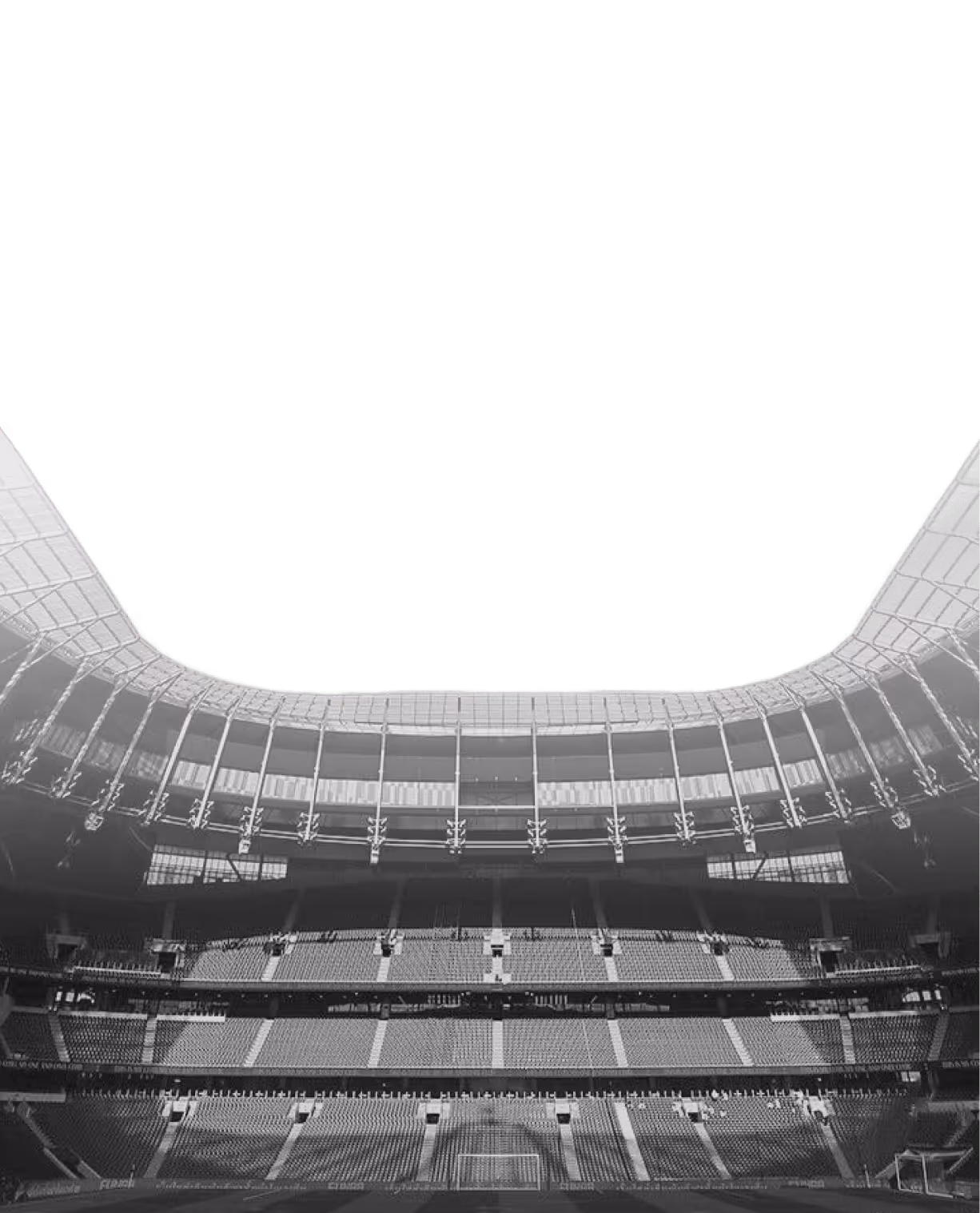 Black and white photo of empty multi-tiered soccer stadium seating and roof structure.