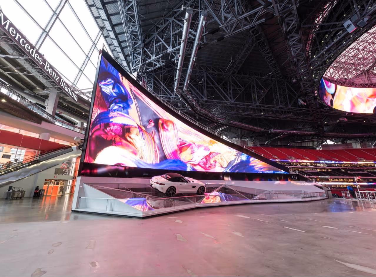 White Mercedes sports car displayed under a large colorful screen inside Mercedes-Benz Stadium.