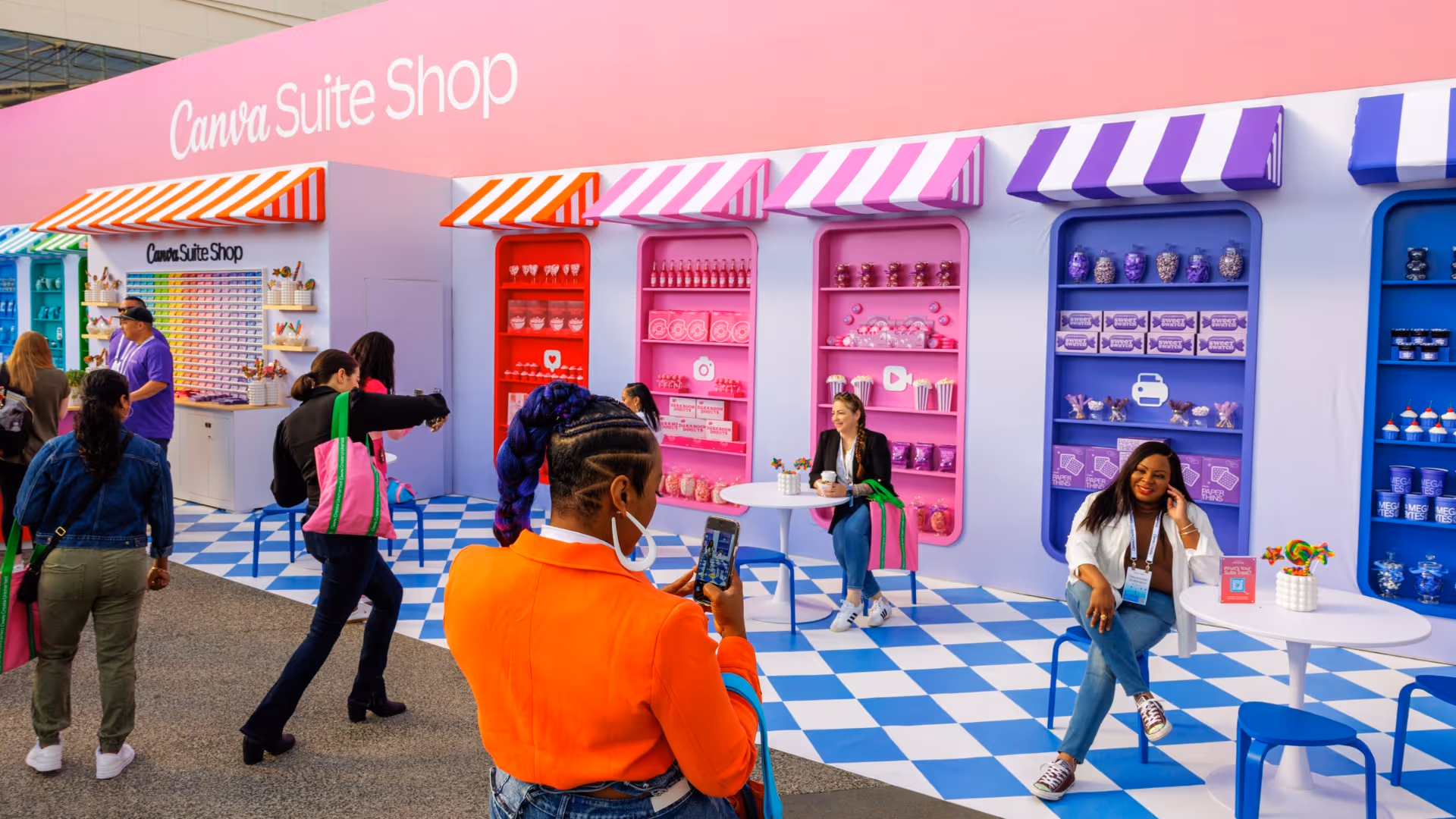 People at colorful Canva Suite Shop with striped canopies, shelves of candy, and blue checkered floor.