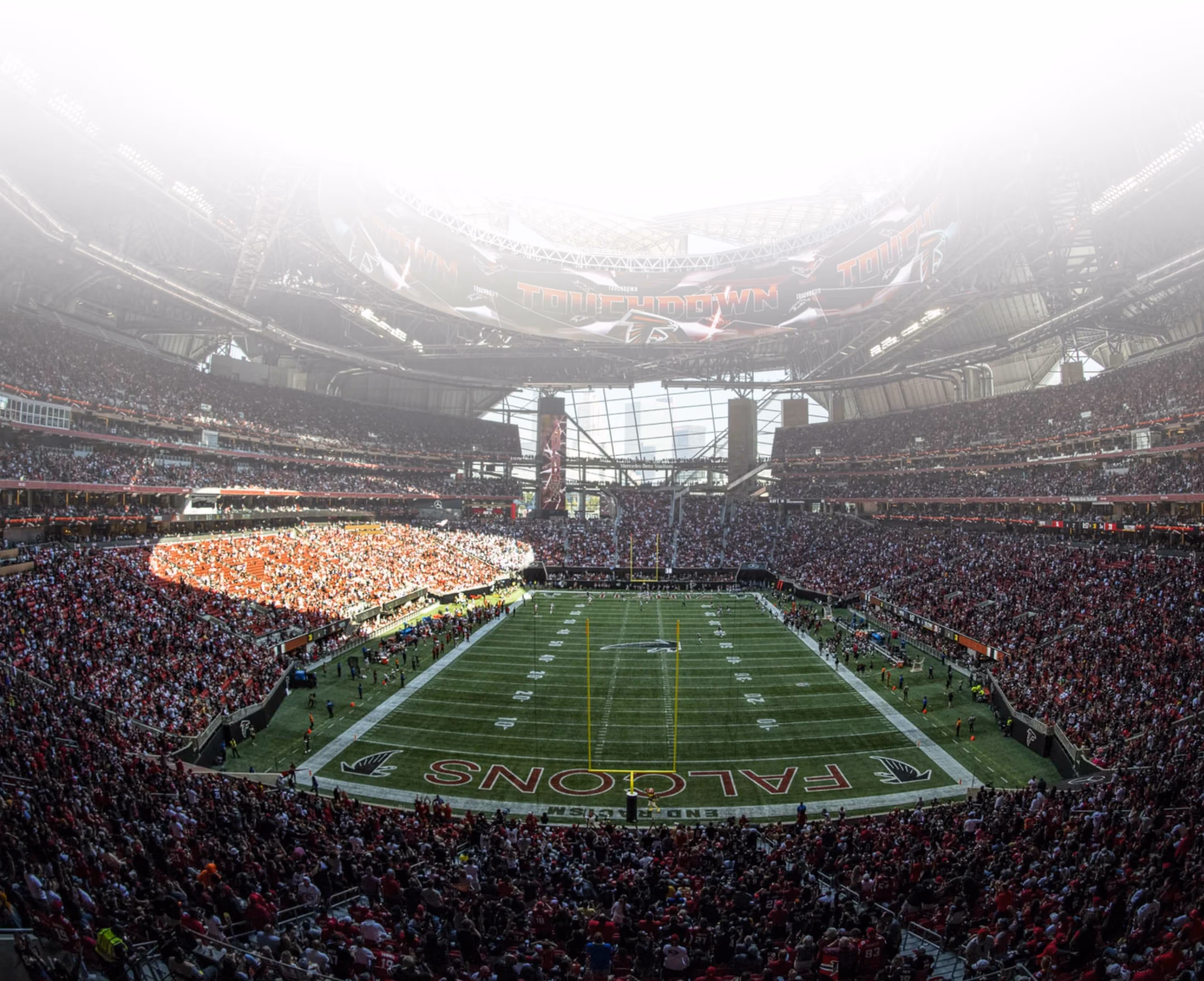 Crowd cheering with raised hands at a daytime football game in a large stadium.