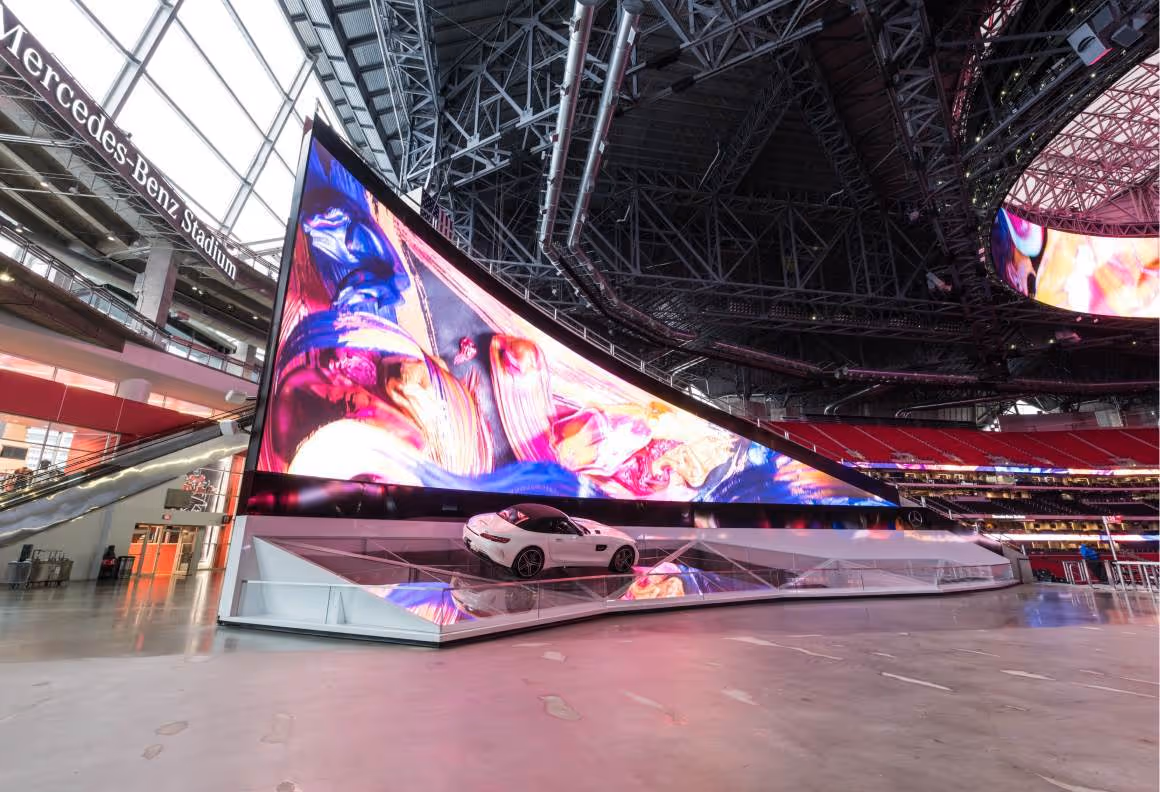 White sports car display under large vibrant screen inside Mercedes-Benz Stadium concourse.