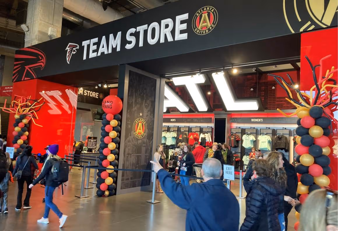 People entering Atlanta United FC team store decorated with black, red, and gold balloons for grand opening.