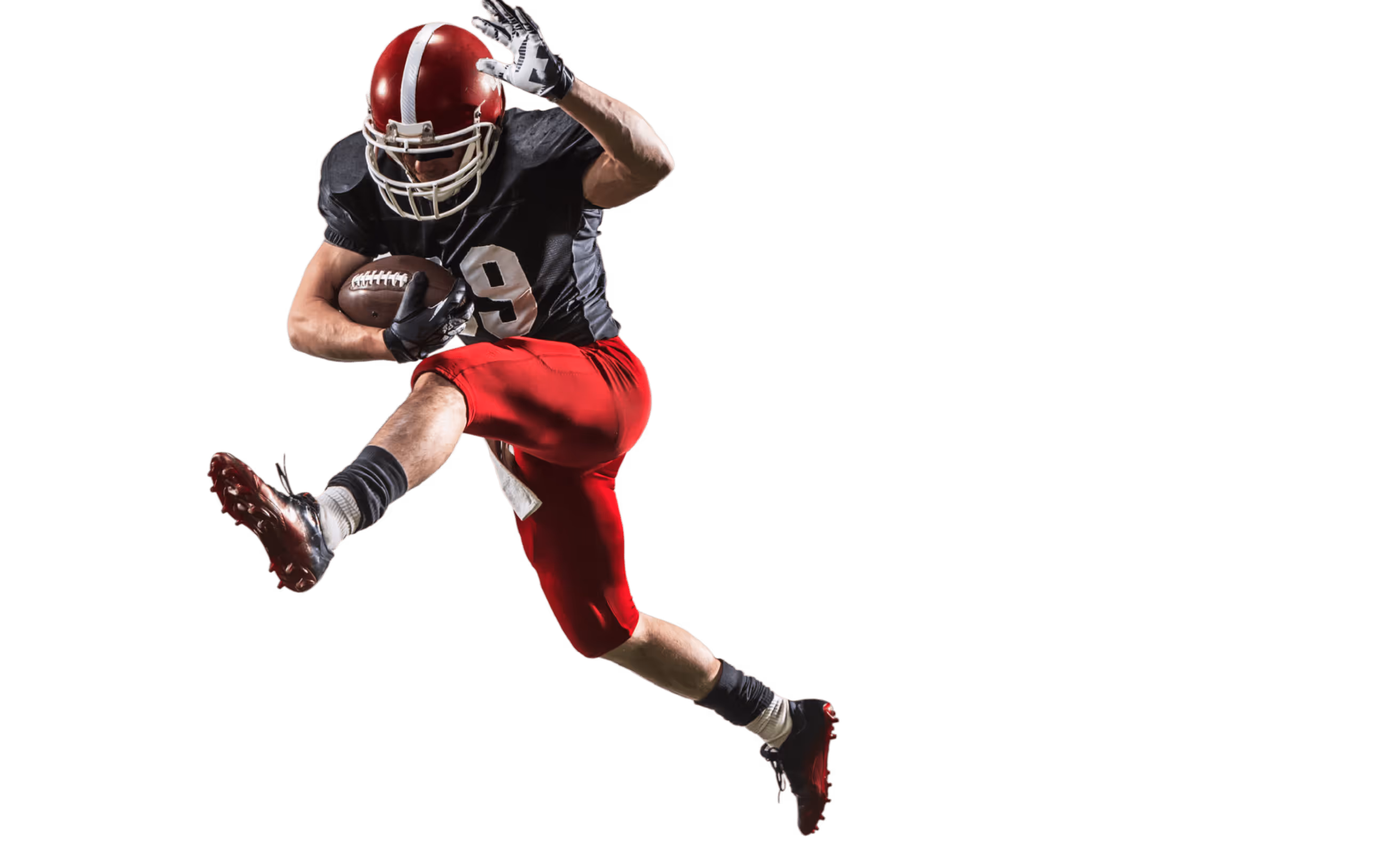 American football player in red helmet and pants leaps holding ball during a play.