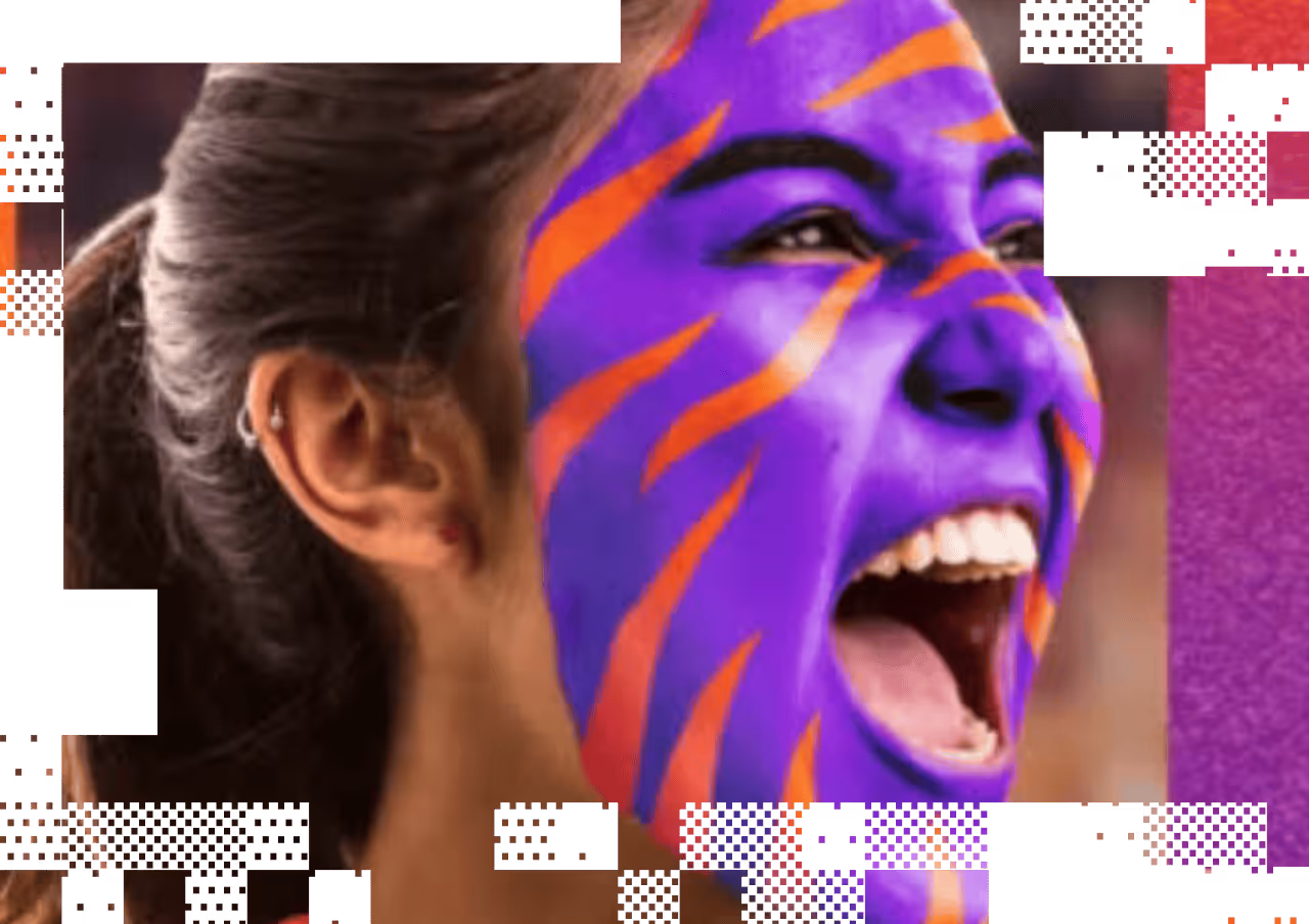 Person with face painted purple and orange cheering with mouth open wide.