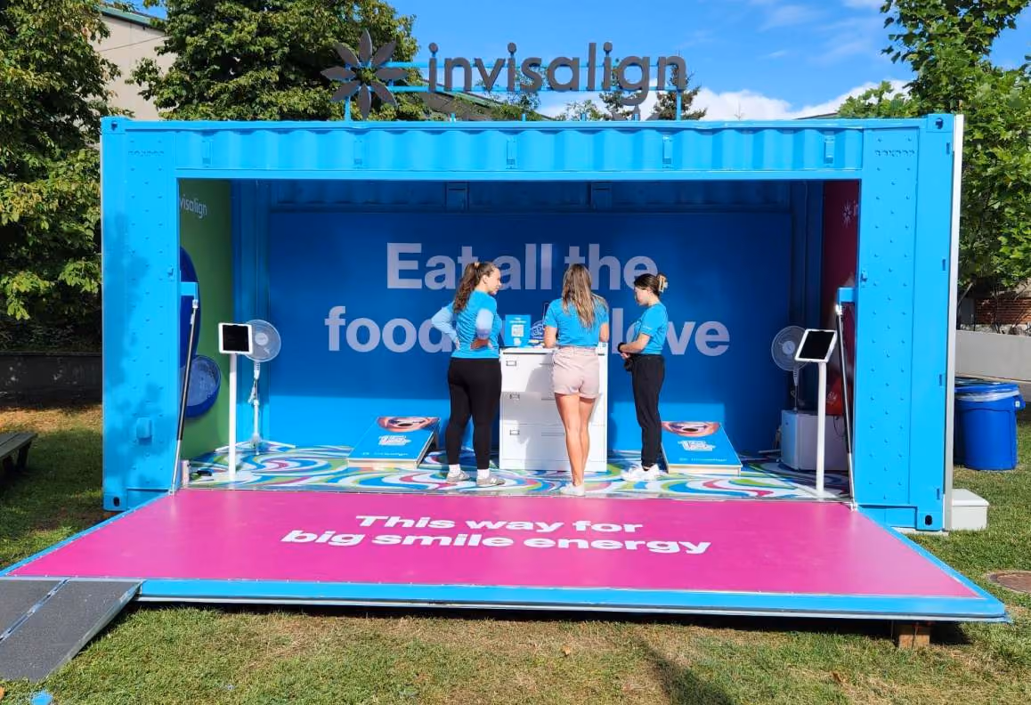 Three women stand inside a blue Invisalign booth with signs encouraging eating all the foods you love.