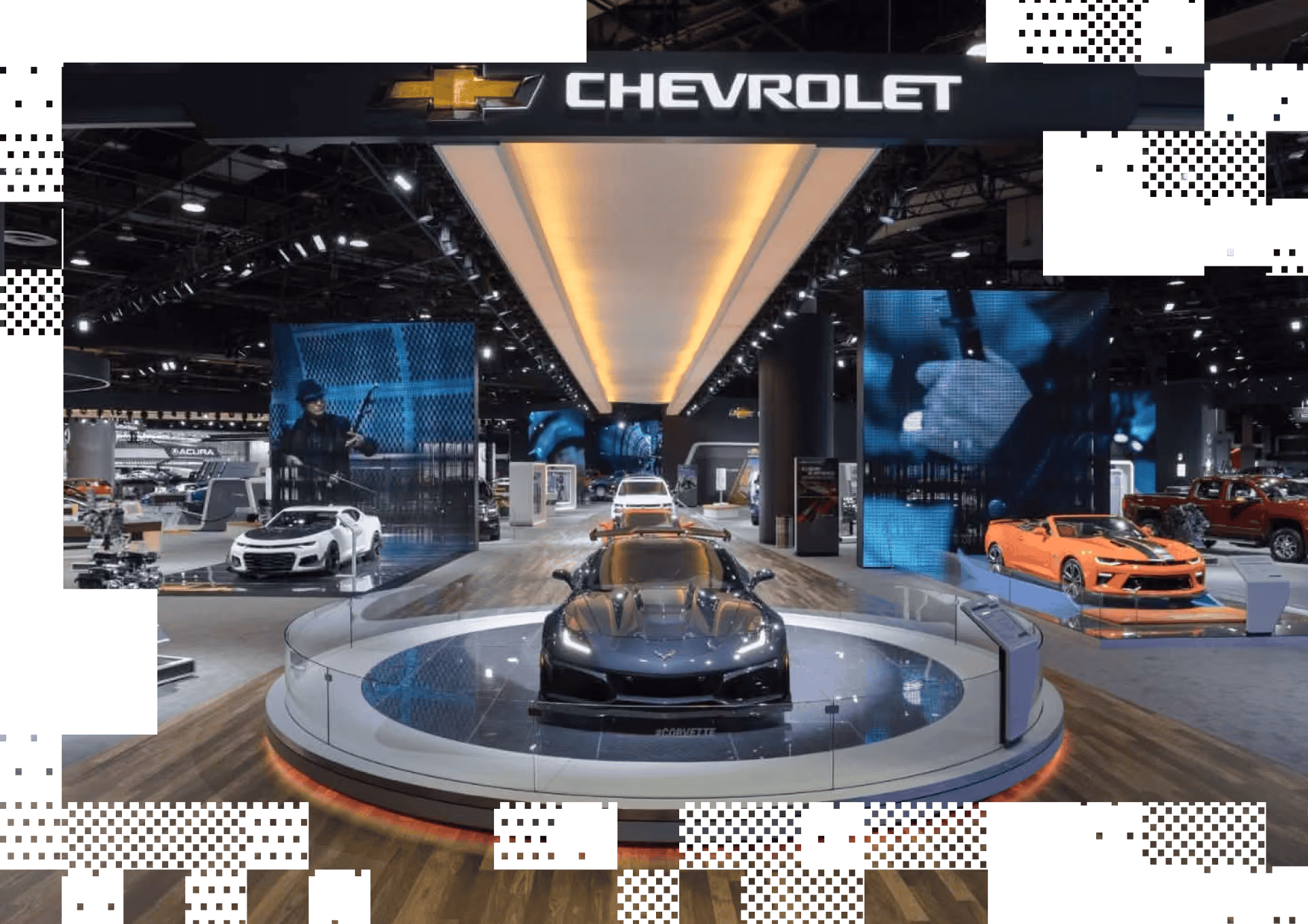 Chevrolet auto show display with black Corvette, white, and orange sports cars surrounded by screens.
