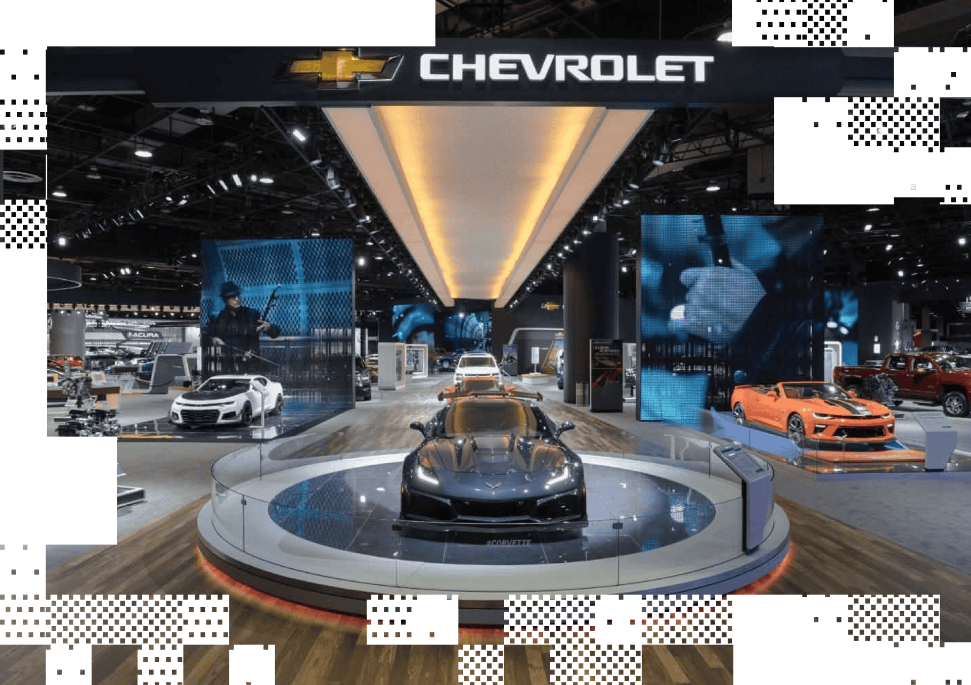 Chevrolet auto show display with black Corvette, white, and orange sports cars surrounded by screens.