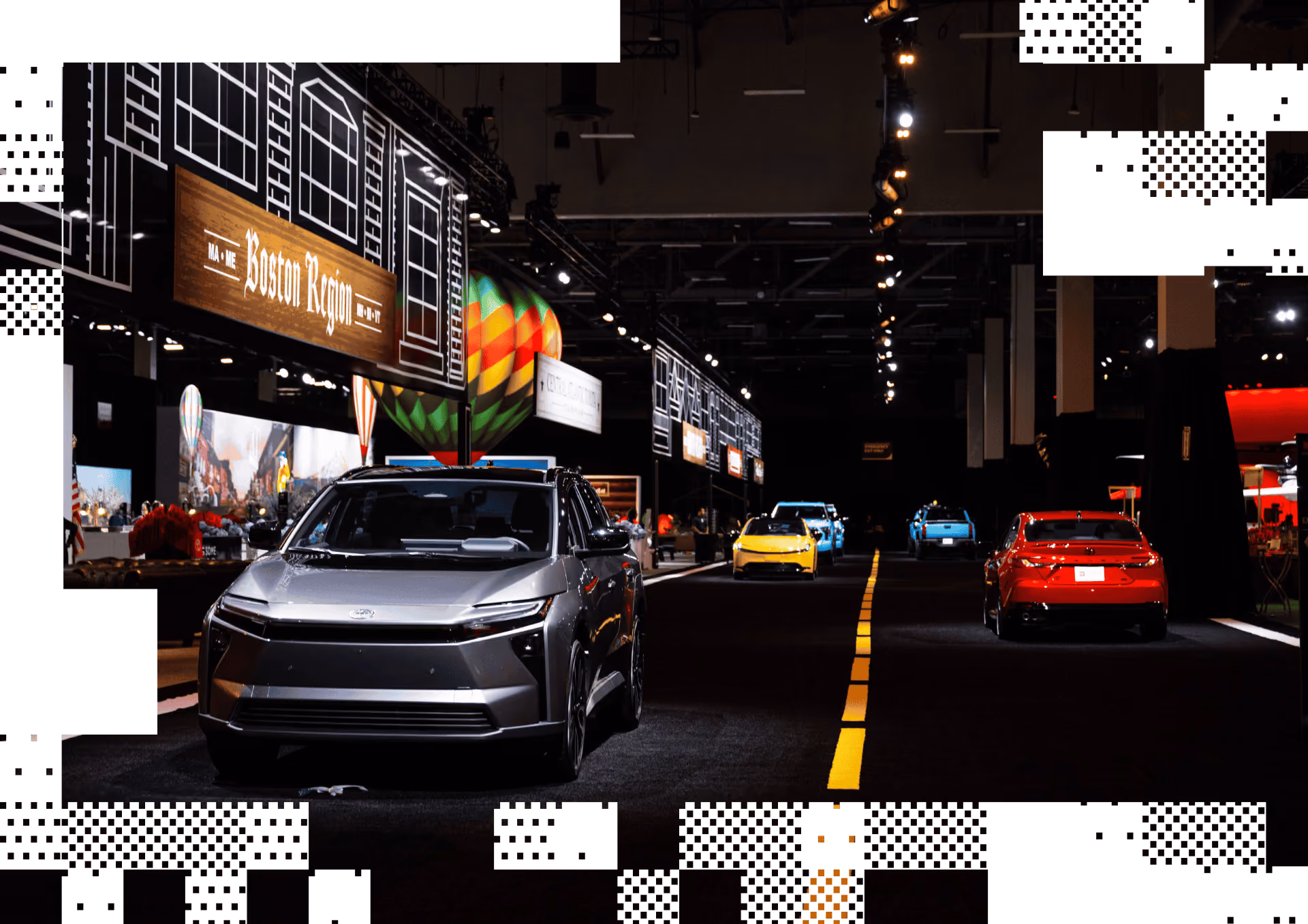 Modern cars displayed along a dark indoor road with signs reading Boston Region above.