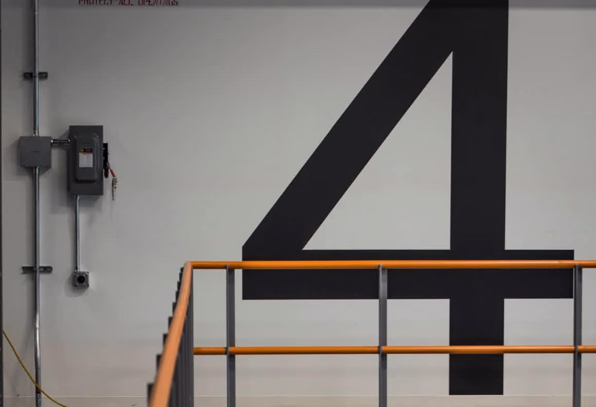Large black number 4 painted on white wall behind orange and gray industrial railing.