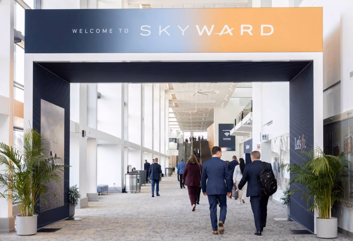 People walking through a black and orange archway with Welcome to Skyward text in a conference hall.
