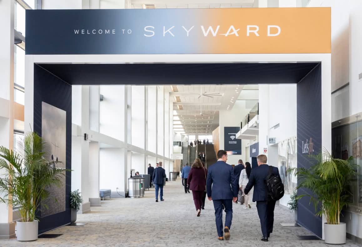People walking through a black and orange archway with Welcome to Skyward text in a conference hall.