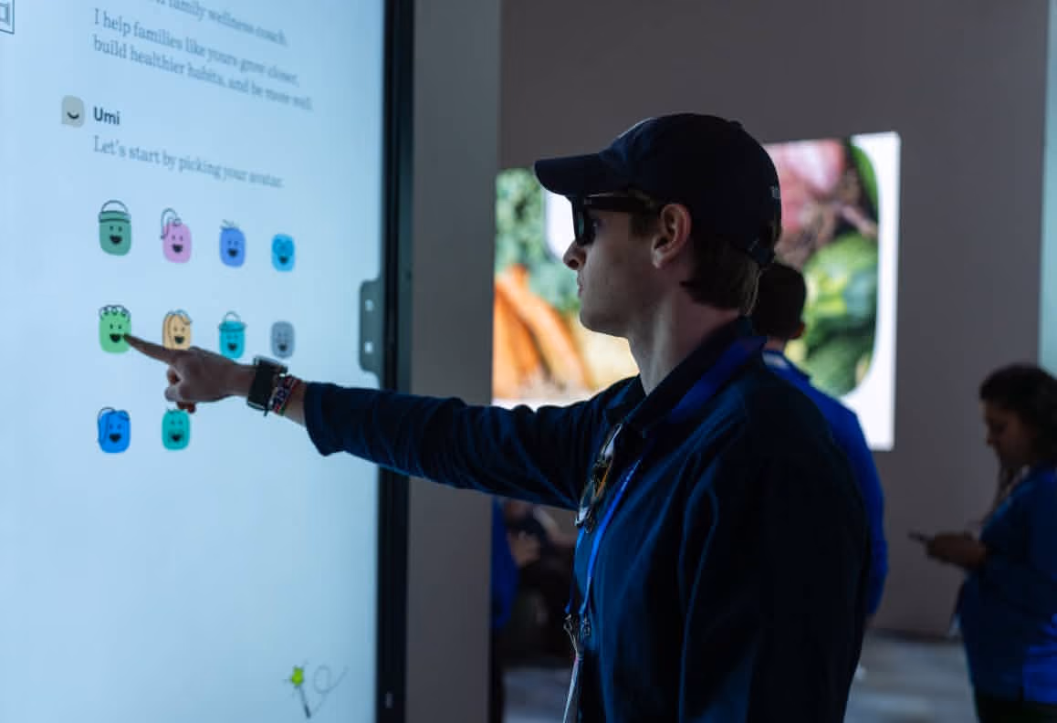 Man wearing a cap and sunglasses interacts with a touchscreen displaying colorful emoji icons.