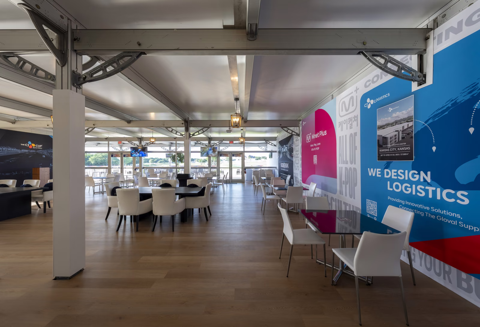 Interior of a CJ Cup Byron Nelson hospitality structure with exposed steel trusses, dining tables and CJ brand graphics