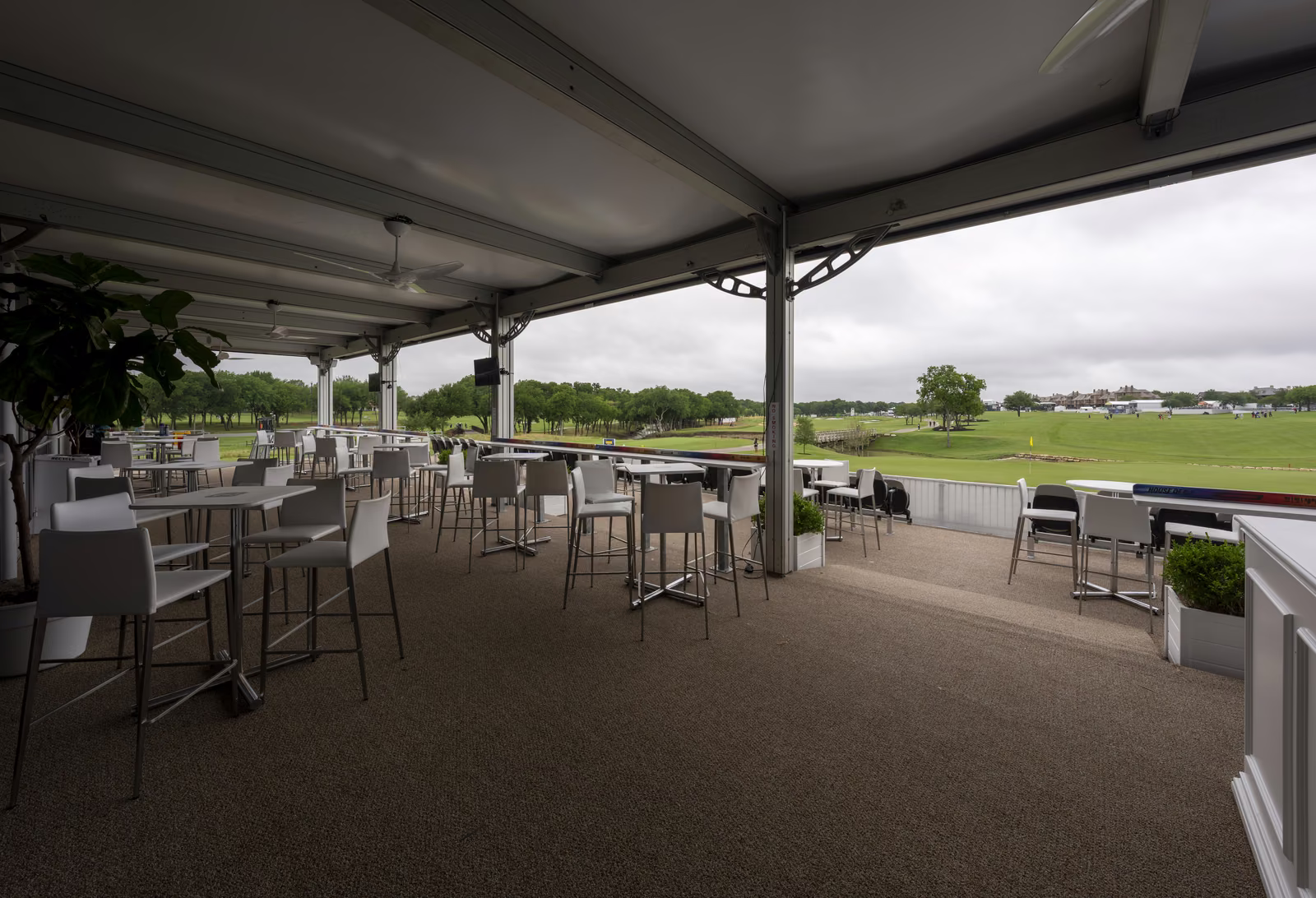 Covered lower-deck lounge at the CJ Cup Byron Nelson with high-top tables and an open view across the course