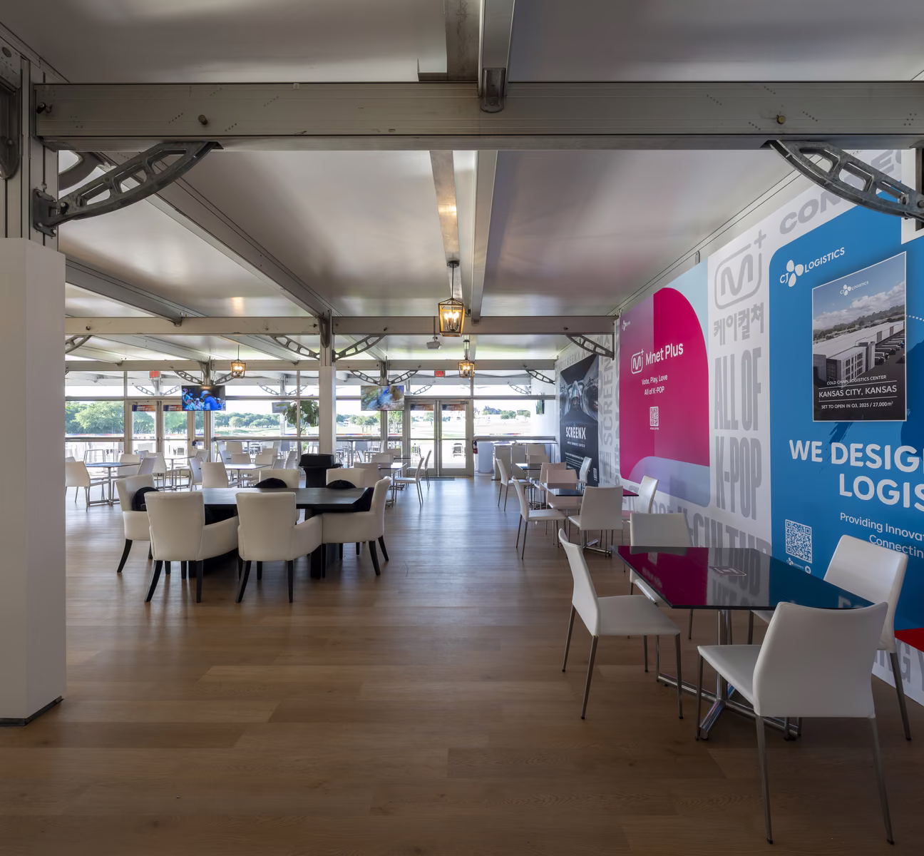 Interior of a CJ Cup Byron Nelson hospitality structure with exposed steel trusses, dining tables and CJ brand graphics