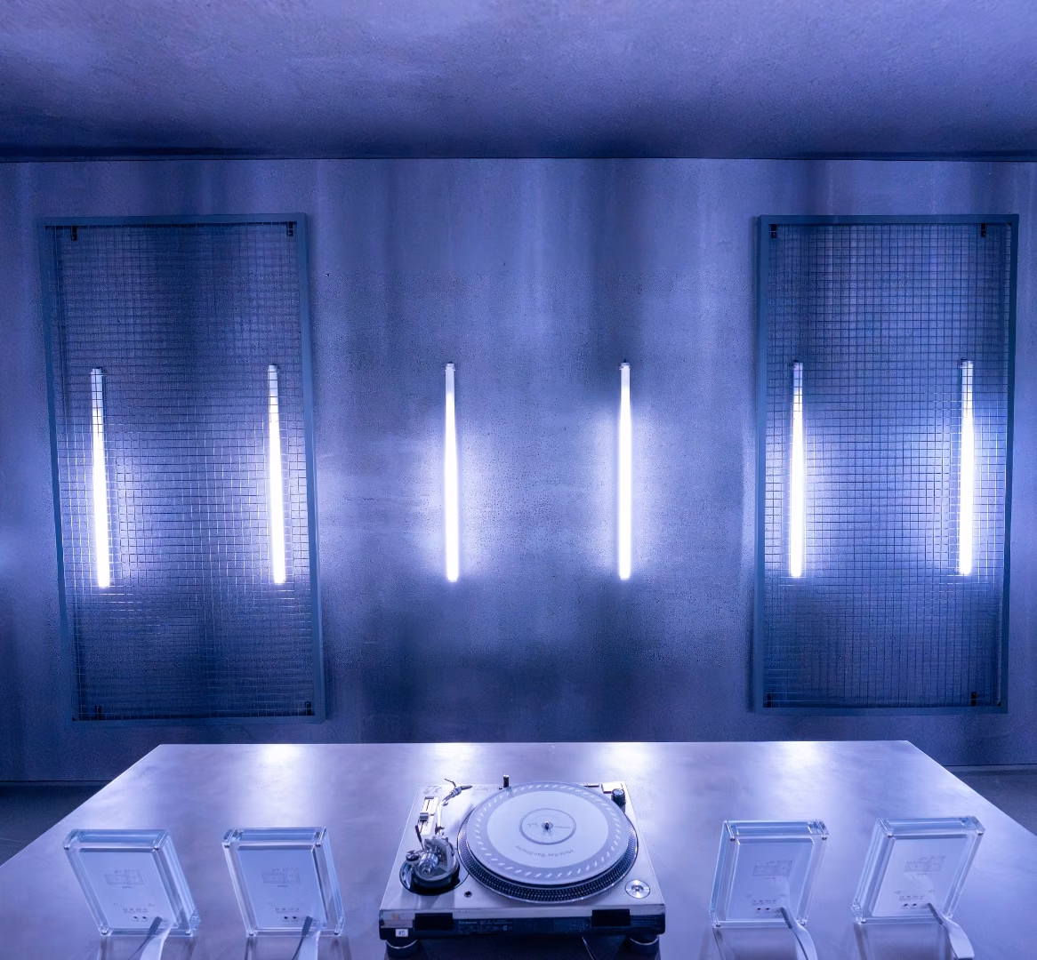 Blue-lit listening room inside the Meta Lab with a turntable on a central table and vertical light tubes on the wall