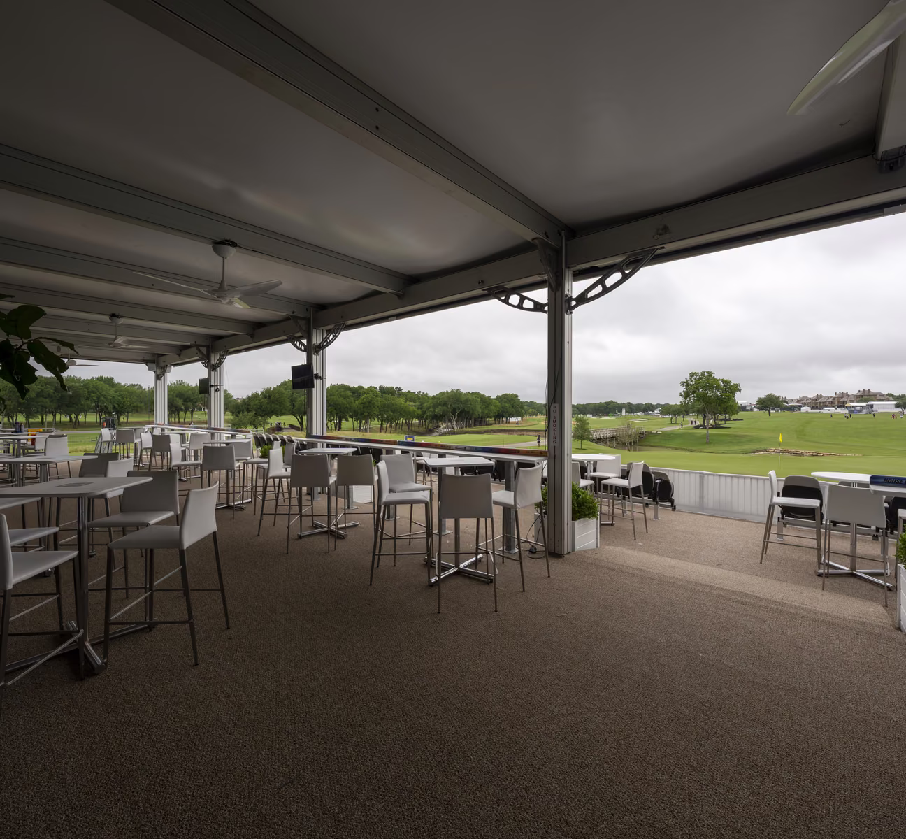 Covered lower-deck lounge at the CJ Cup Byron Nelson with high-top tables and an open view across the course